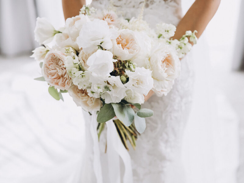 young girl in a white wedding dress holds in her hands a bouquet of flowers and greenery with a ribbon