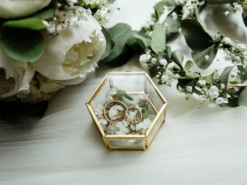 Wedding details. two classic gold wedding rings in a glass box and a bouquet of white flowers and greenery.