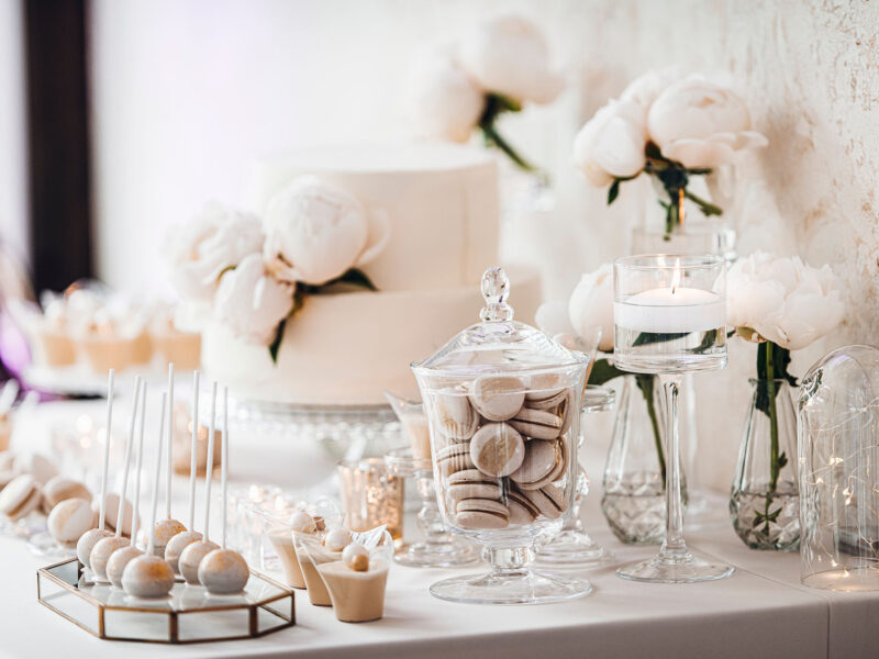 White wedding cake decorated by flowers standing on festive table with lots of snacks on side. Wedding Recetion